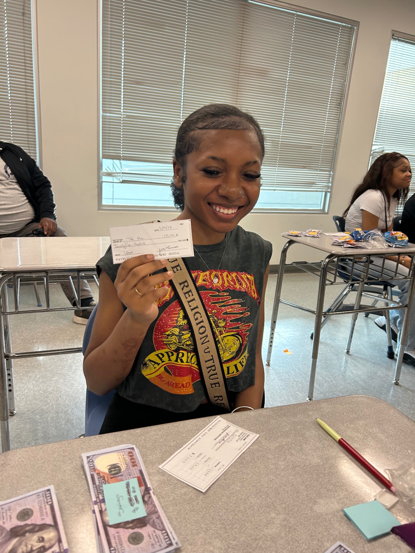 Student smiling while holding a check during a Jus One Academy classroom session